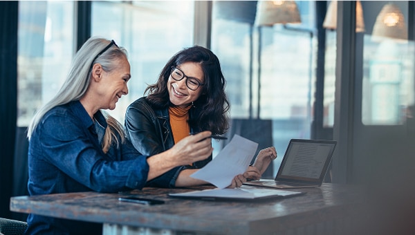 Two women at a desk talking over documents.