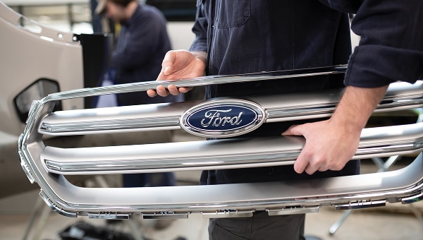 A person handling the grill of a Ford vehicle.