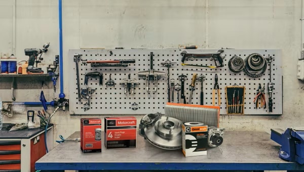 Collection of auto parts positioned in front of various tools hanging on a pegboard.