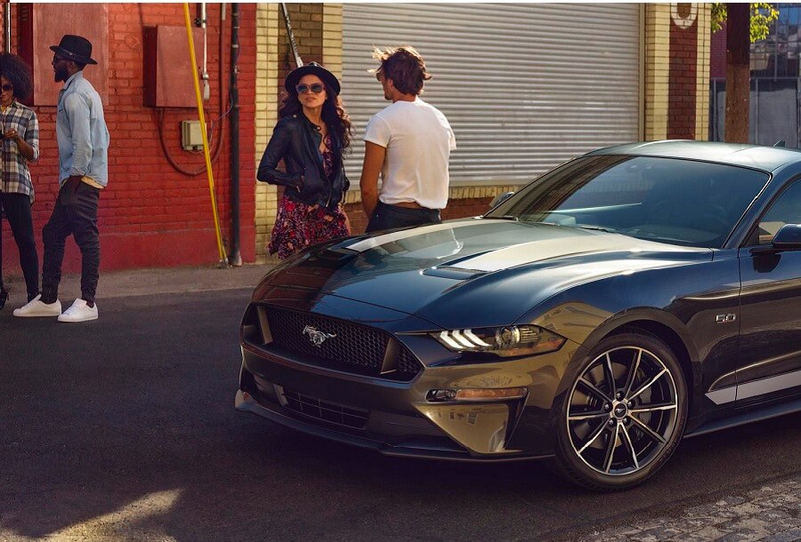 2023 Ford Mustang® coupe in Carbonized Gray Metallic parked on the street with four people standing nearby