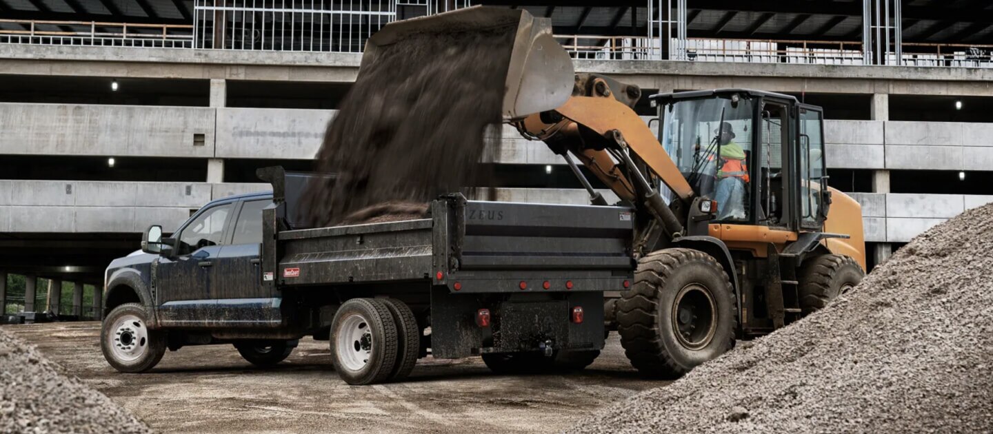 Ford chassis cab getting dirt dumped into bed by bulldozer