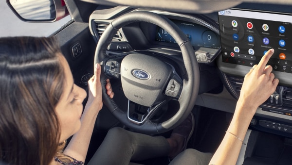 A woman seated in a 2024 Ford Escape interacting with icons on a dash-mounted touchscreen