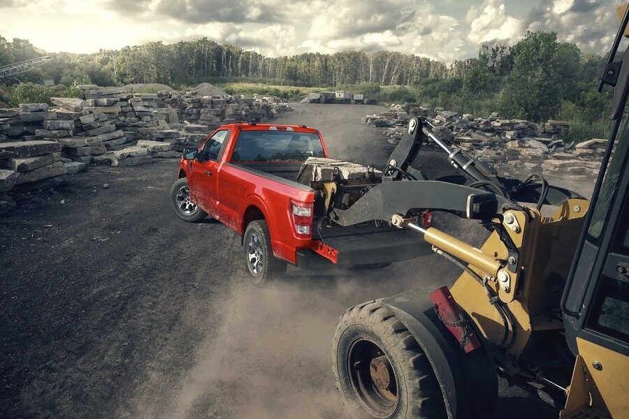 Red 2024 F-150 Ford Truck Towing large construction equipment