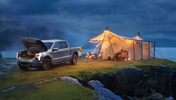 A dark gray 2024 Ford F-150 Lightning pickup truck parked next to a tent on a rocky landscape