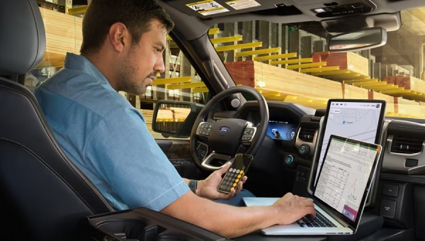 A man behind the wheel of a parked 2024 Ford F-150 Lightning pickup truck. He is using the interior work surface as a desk