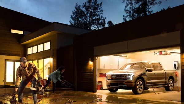 A man and a woman clean up fallen branches in the driveway showing a 2024 Ford F-150 Lightning