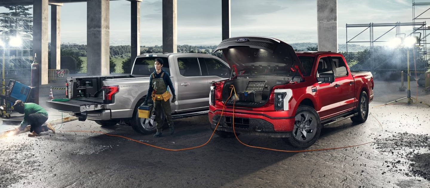 Woman charging an F-150 Lightning on construction site next to another F-150 Lightning.