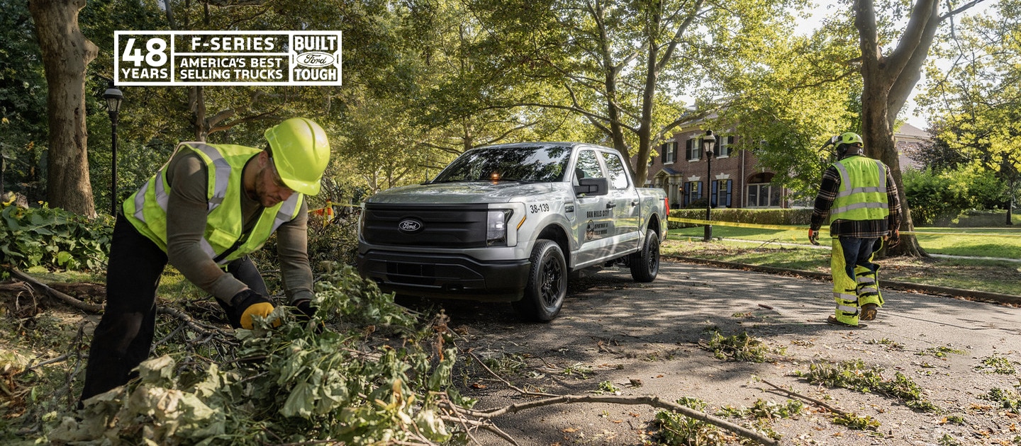 An F-150 Lightning in the background of workers cutting trees