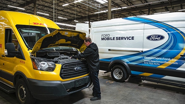 Mobile Service technician working under the hood of a yellow DHL Express van next to a Ford Pro Mobile Service van.