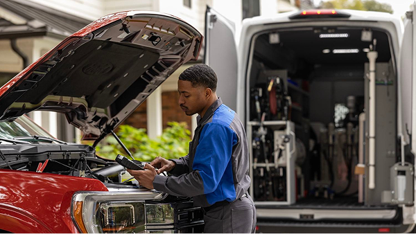 Technician performing engine maintenance on a red Ford truck in indoor service area.