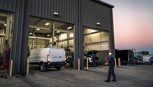 White Ford Pro van entering a commercial service center at sunset while a technician walks nearby.