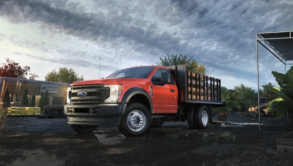 Driver using a upfitted red flatbed truck on a paved road.