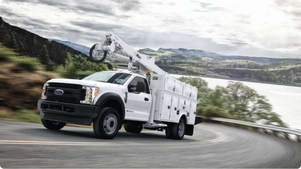 A white Ford utility truck travels along a road next to a river