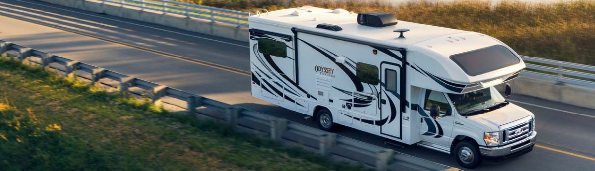 White Odessey RV with blue accents driving down the road.