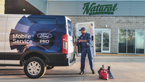 Ford Pro Mobile Service technician working at the back of a branded Ford Transit van parked at a customer location.