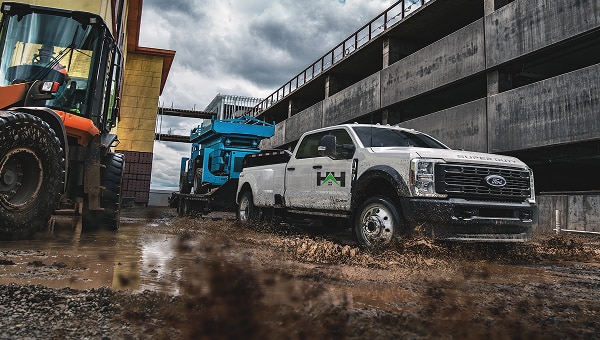 Duty truck towing a heavy machinery trailer through a muddy construction site.