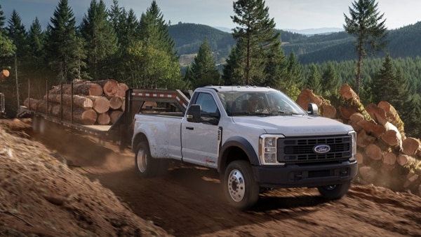 2026 Super Duty F-450 XL model with the STX Appearance Package pulling a trailer of tree trunks on a dirt road