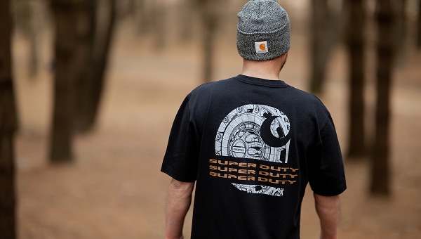 Rear view of a man wearing a black t-shirt with a "Super Duty" graphic in a wooded setting.